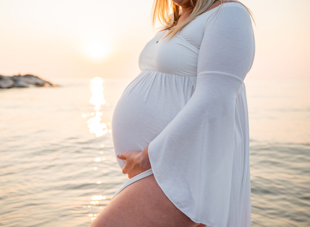 Pregnant woman gently holding her baby bump at sunset by the beach
