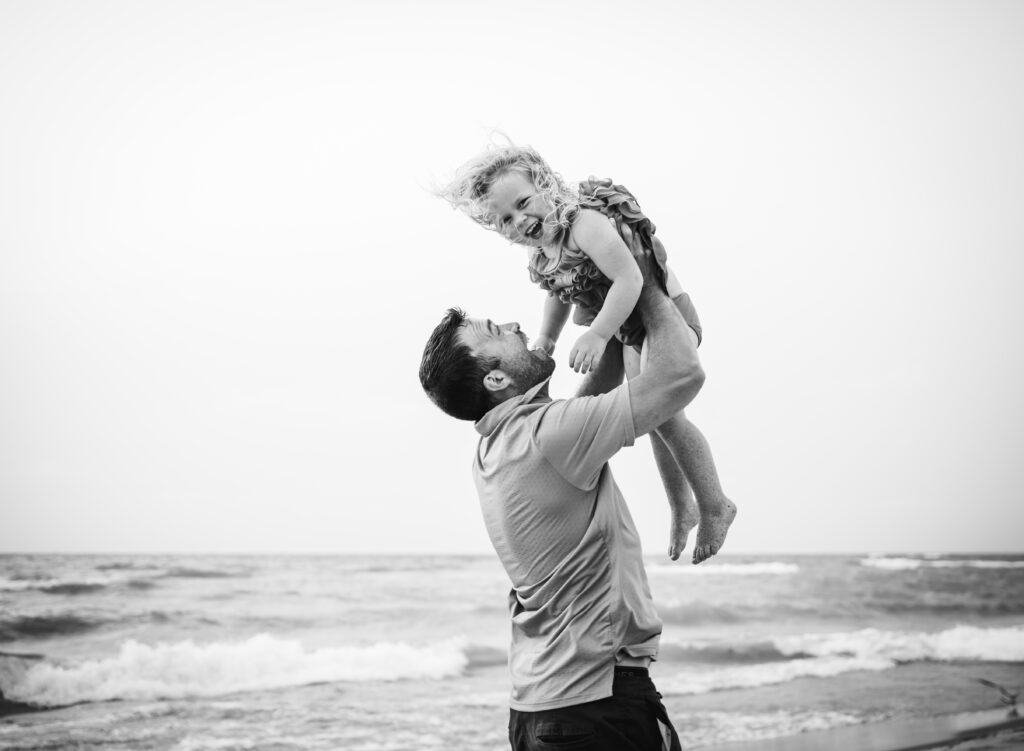 Dad holding his smiling daughter high at the beach - family photo by Leslie Q Photography